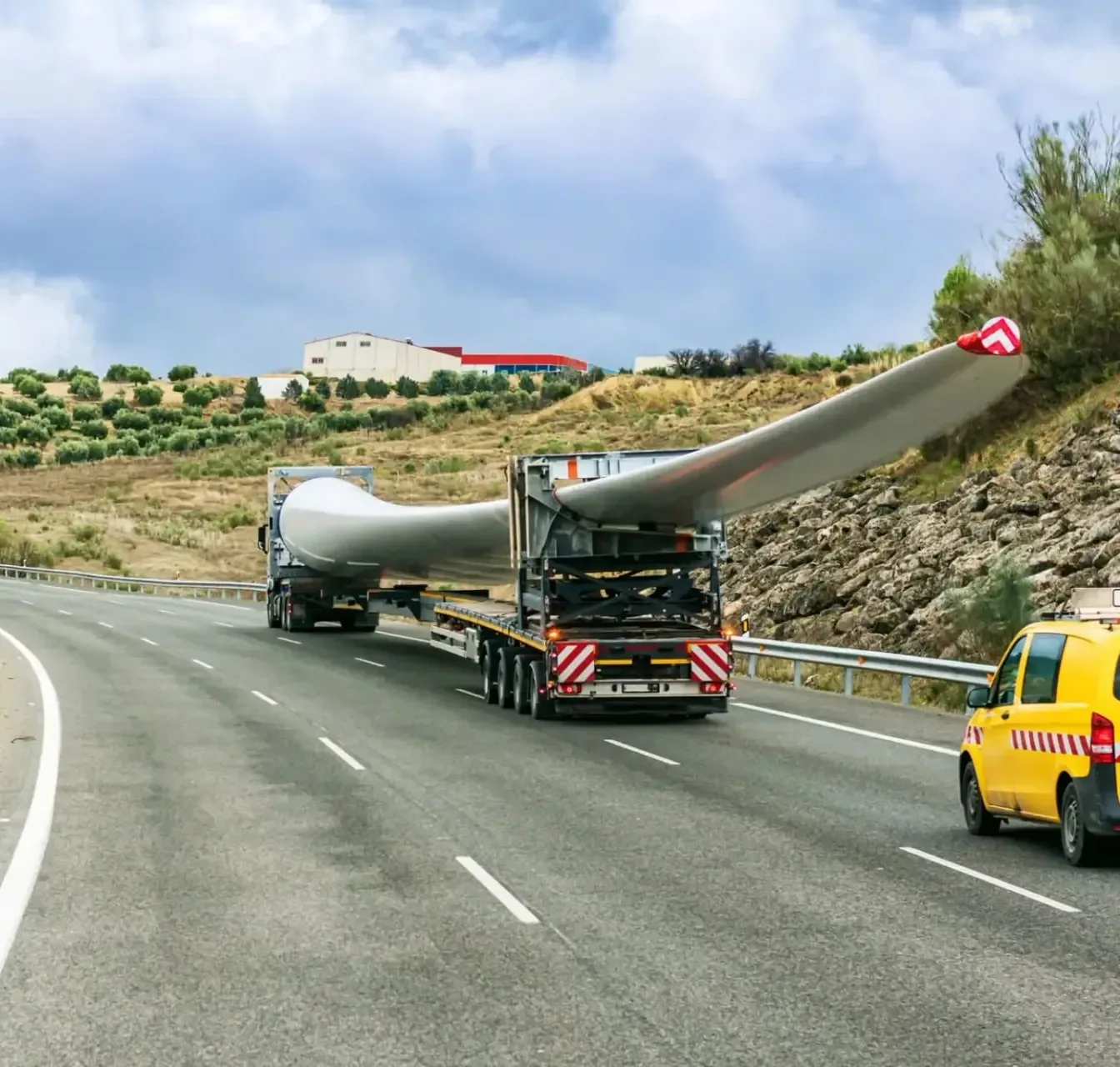 Pale de turbină eoliană pe trailere extensibile, în convoi pe drum, cu vehicul de escortă